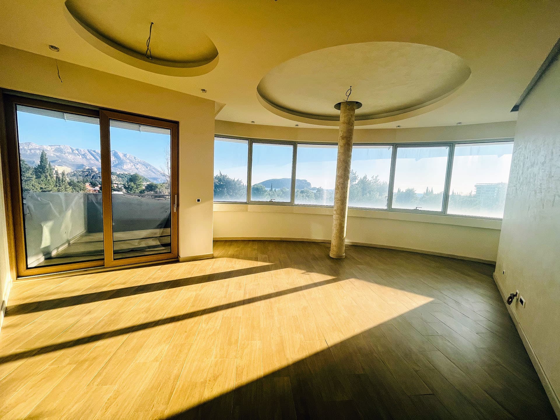 Spacious living room in an apartment in Budva, Montenegro, with panoramic windows, mountain views, and a stylish column.