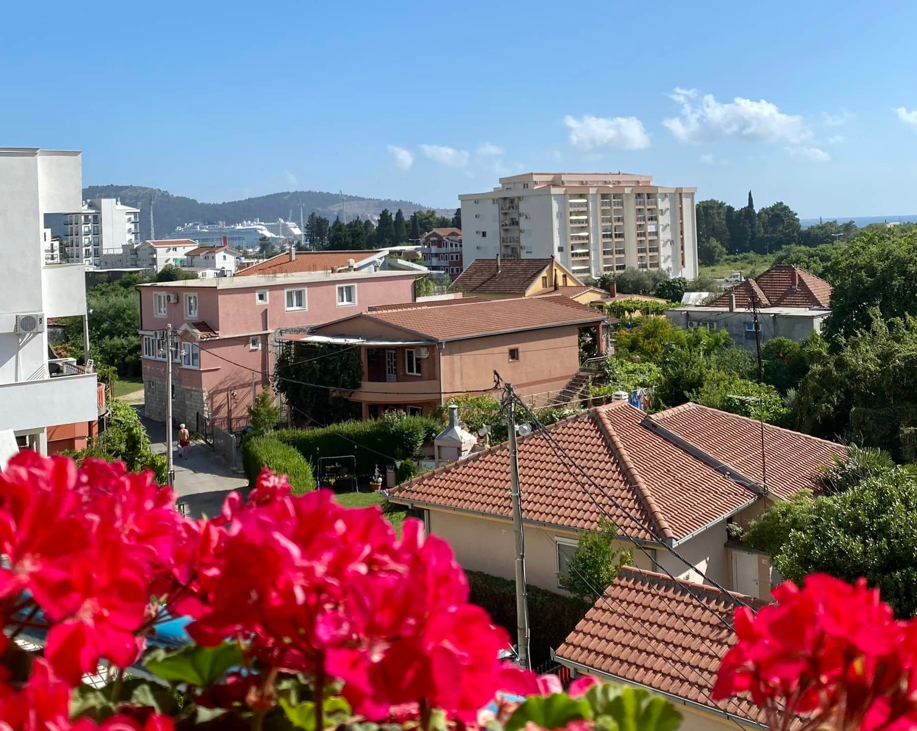 View from the balcony of a house in Shushan, Montenegro: red flowers in the foreground and a panoramic view of the city with tiled roofs.