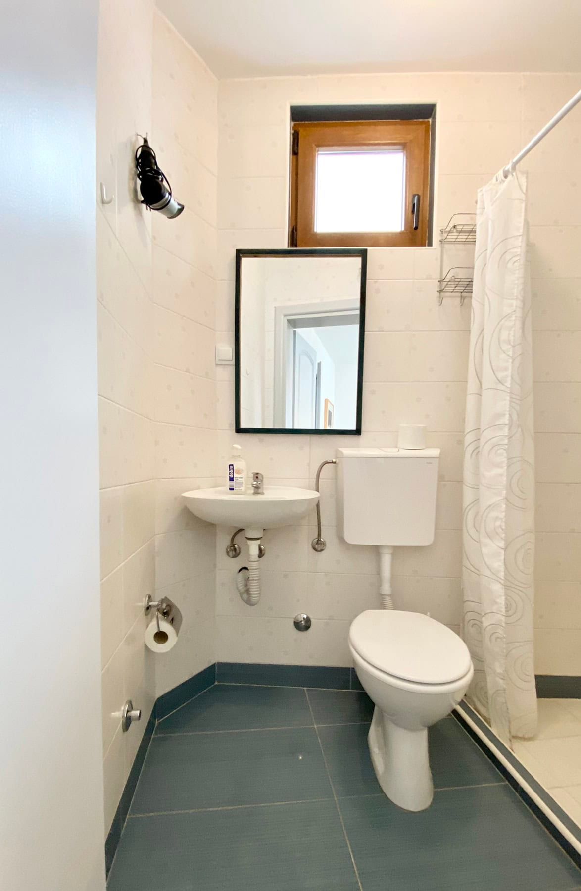 Bright bathroom in a house in Shushan, Montenegro: white fixtures, a shower area, and a window with a wooden frame.