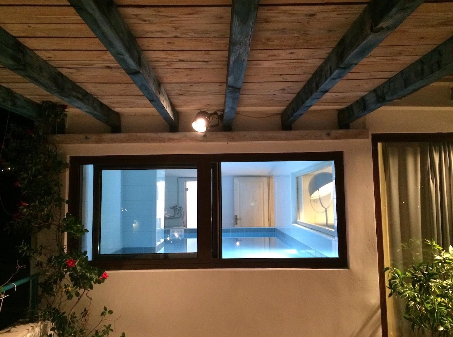 Indoor pool with lighting in a house in Shushan, Montenegro, with a ceiling finished with wooden beams and a panoramic window.