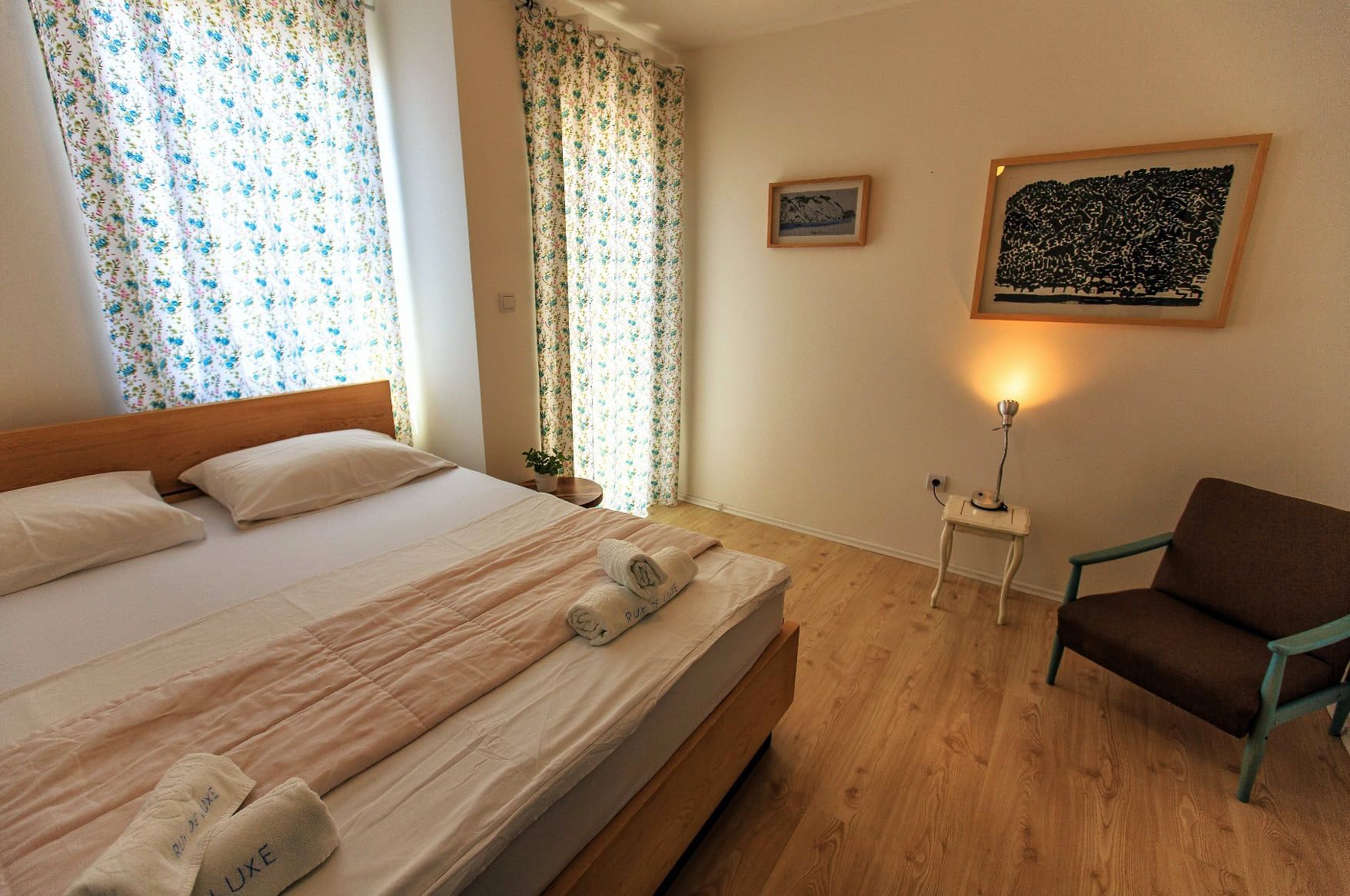 Cozy bedroom with a double bed in a house in Shushan, Montenegro: bright interior, wooden floor, and an armchair.