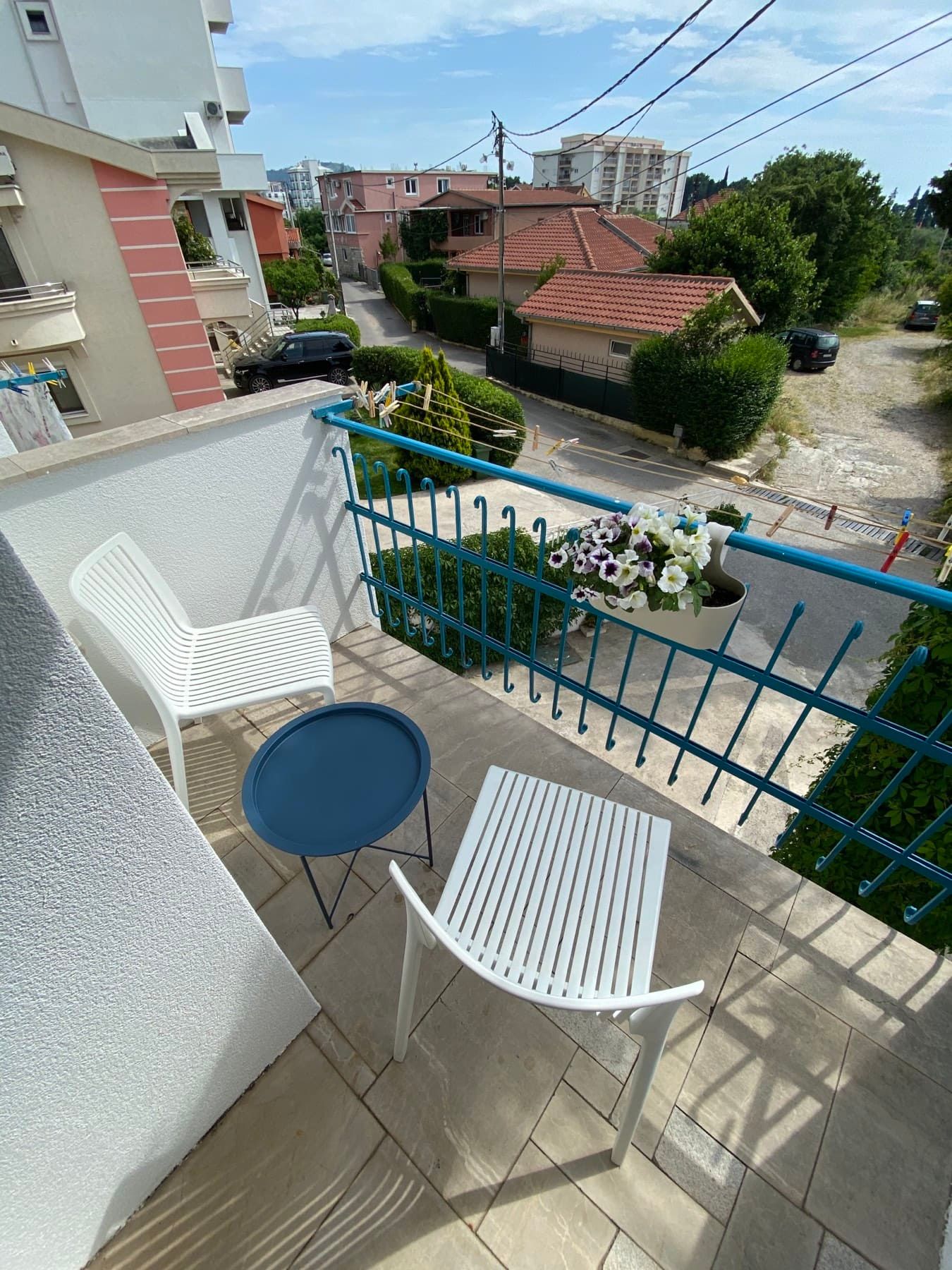 Cozy balcony with white chairs and a table in a house in Shushan, Montenegro, overlooking a residential area and greenery.