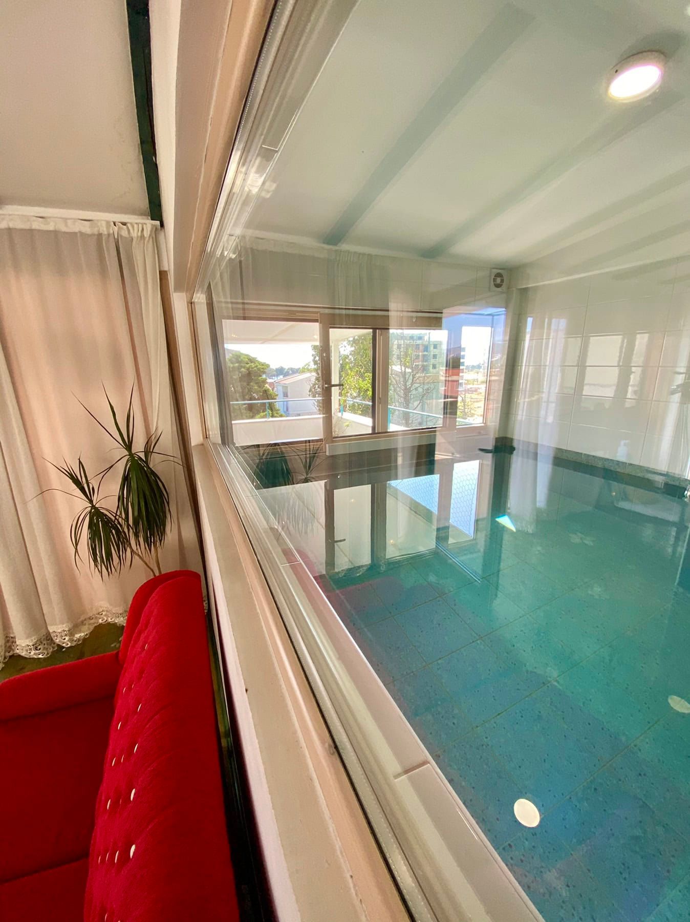Indoor pool with panoramic glazing and a red sofa in the house, Shushan, Montenegro.