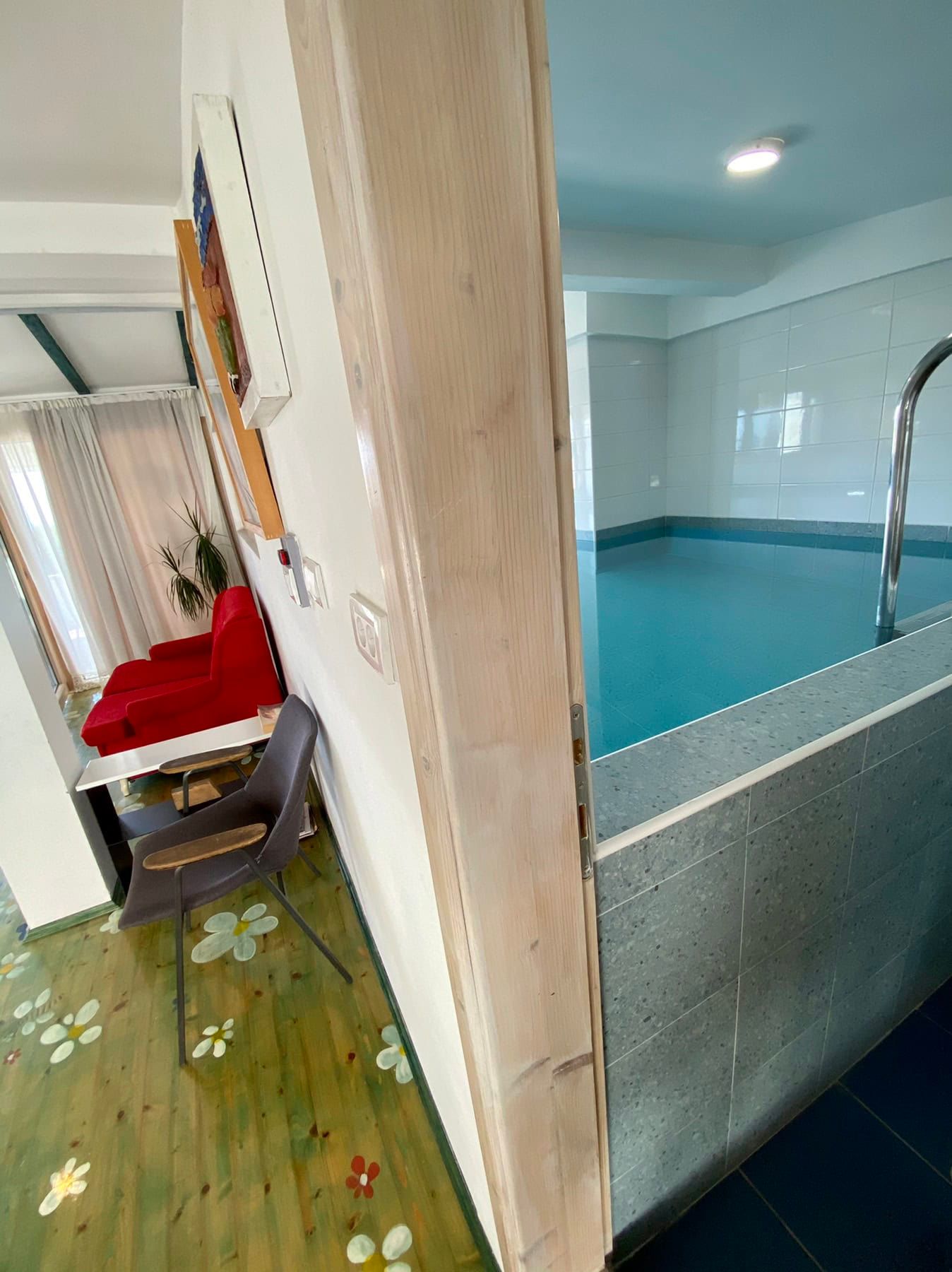 Indoor pool and lounge area with a red chair in the house, Shushan, Montenegro. Interior with tile and wood finishes.