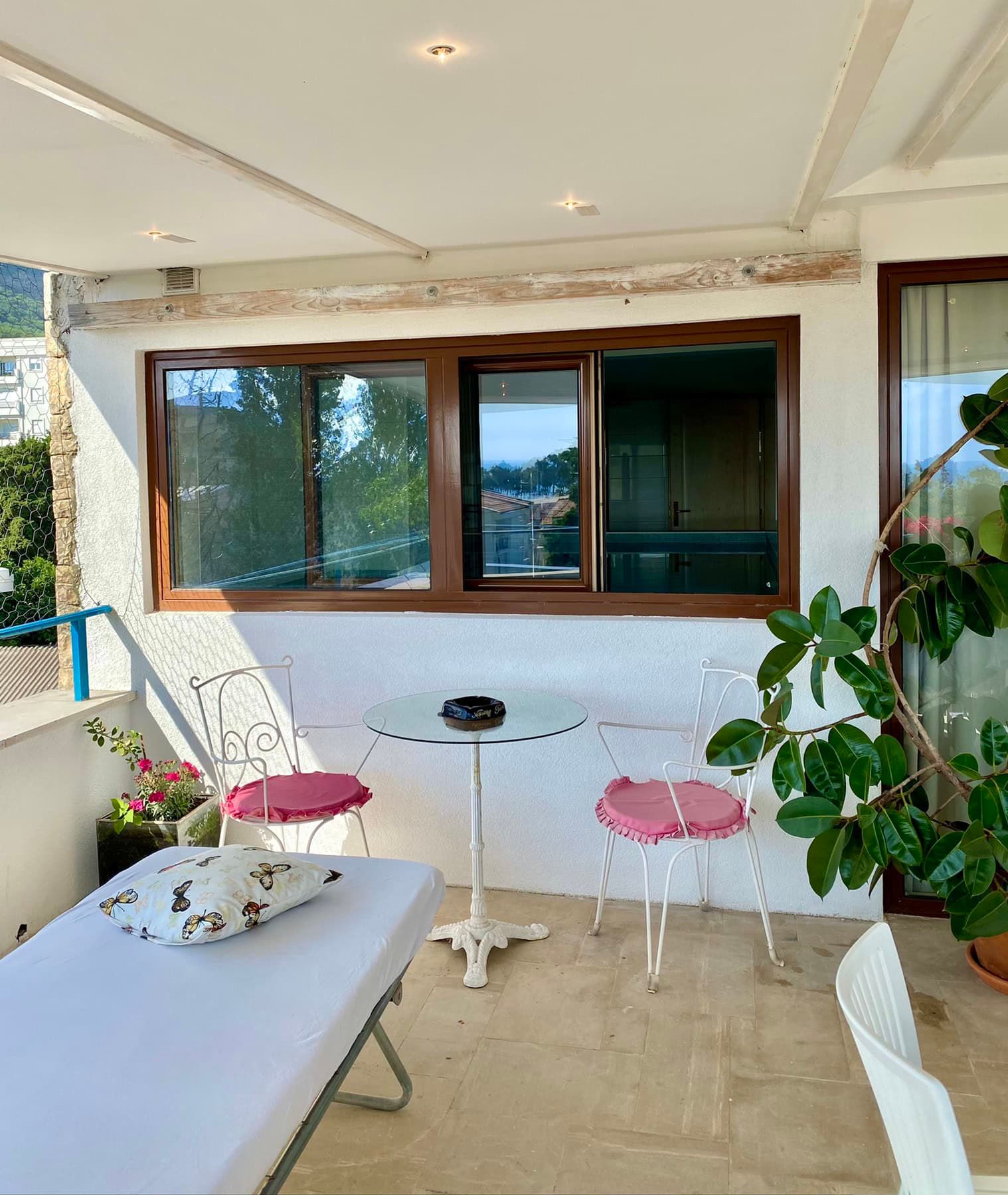 Cozy terrace with wrought-iron furniture and sea view in a house, Šušanj, Montenegro. Bright balcony with plants and a seating area.
