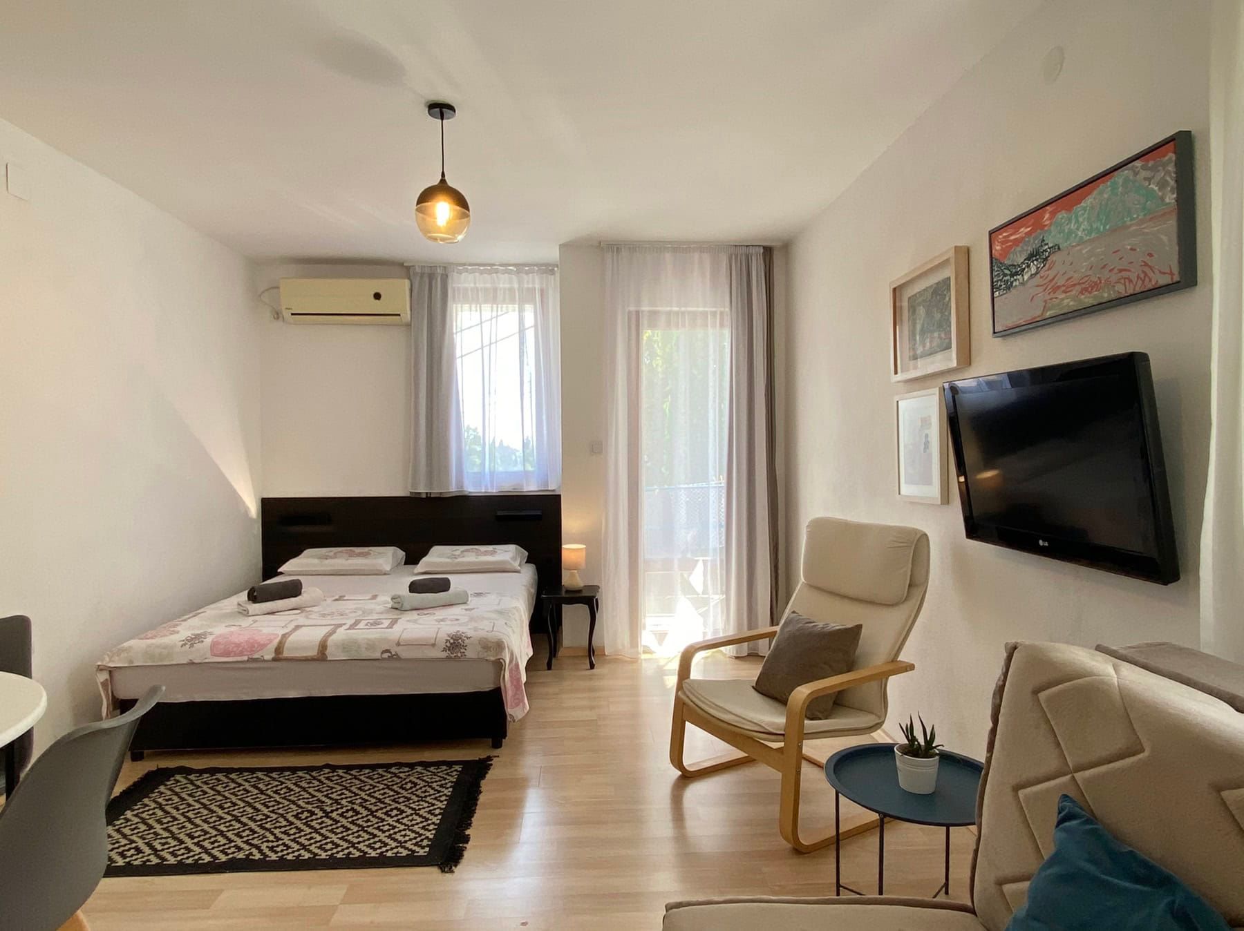 Cozy bedroom in a house in Shushan, Montenegro: double bed, armchair, TV, and access to the balcony with light finishes.