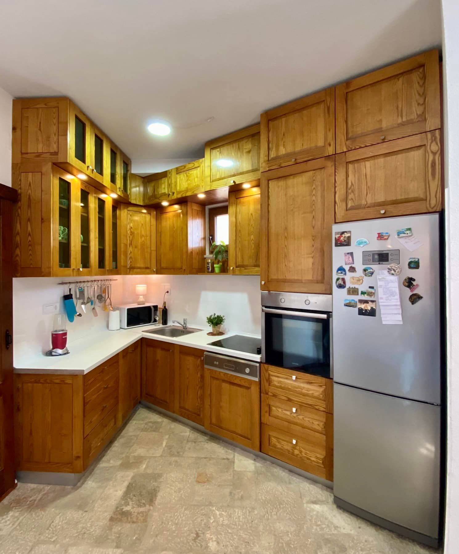 Corner kitchen made of solid wood with modern appliances in a house, Shushan, Montenegro. Light countertop and stone floor.