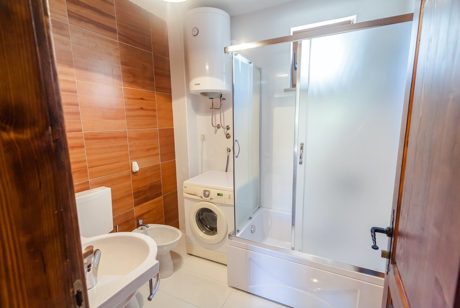 Bathroom in a house in Shushan, Montenegro: shower cabin, washing machine, water heater, and wood-look tile finish.
