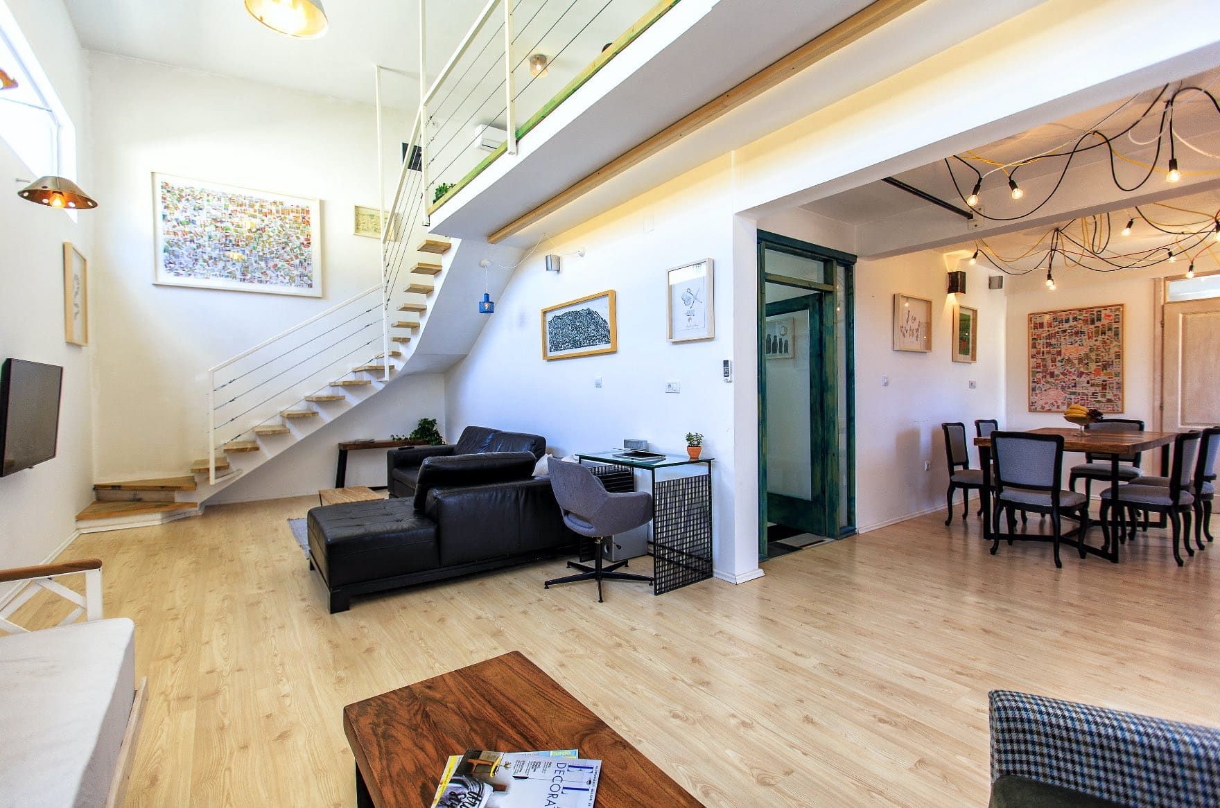 Living room with staircase in a house in Shushan, Montenegro: modern interior, leather sofa, dining area, and light flooring.