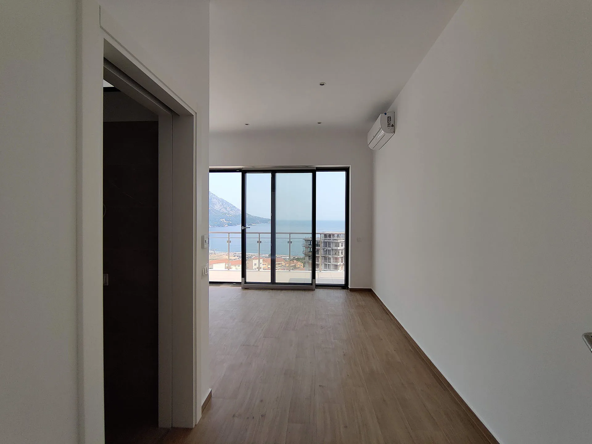 Empty room with wood flooring and large sliding glass doors leading to a balcony with sea view.