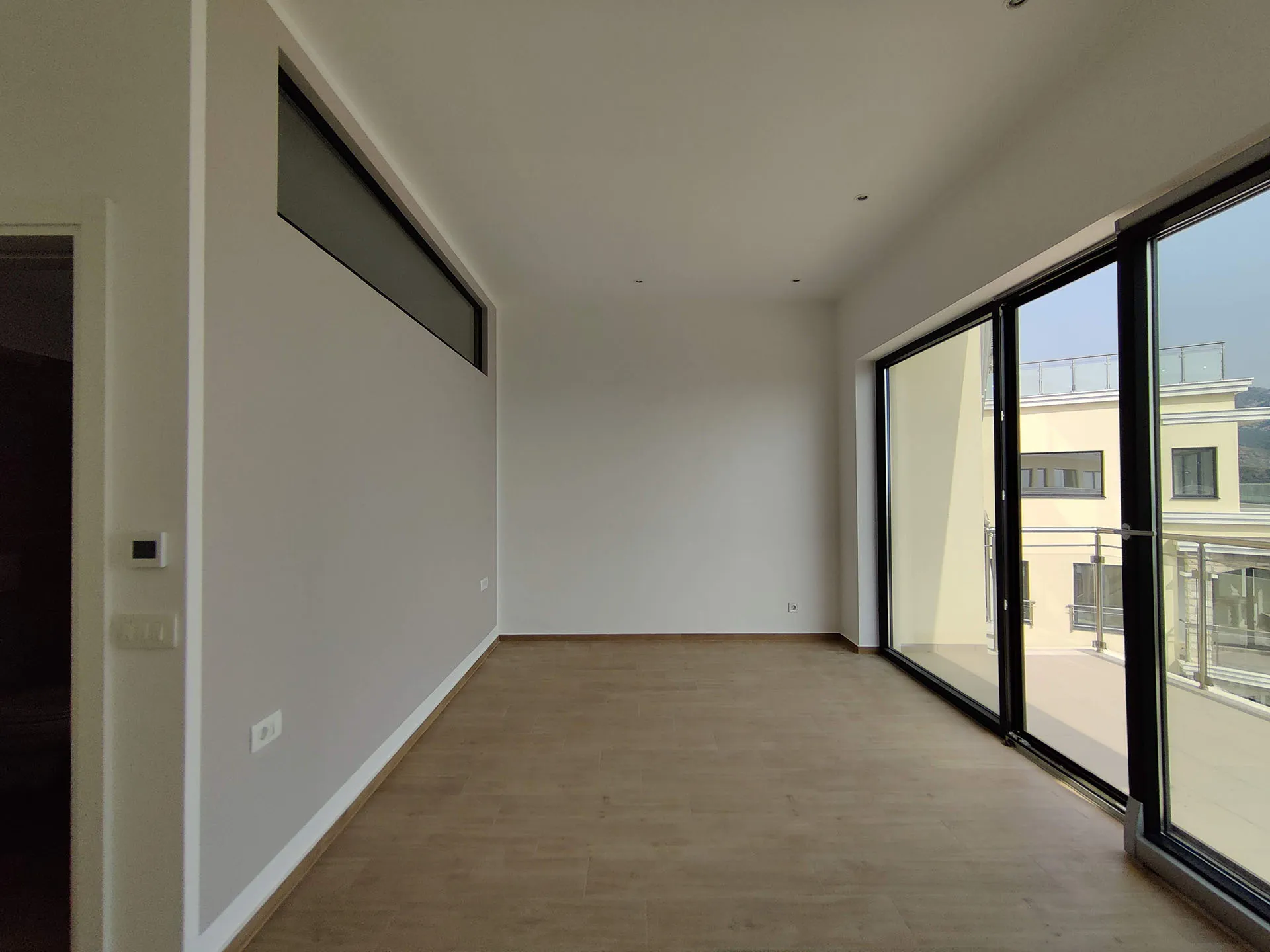 Empty room with light walls, wood-look flooring, and large sliding glass doors leading to an outdoor balcony area.