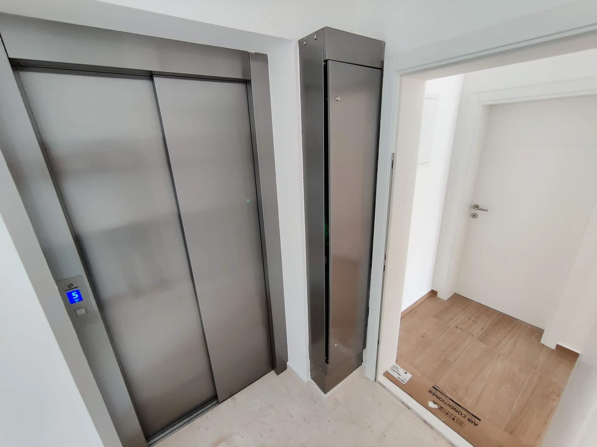 Elevator lobby featuring metallic elevator doors and an open doorway leading to a hallway with wood flooring.