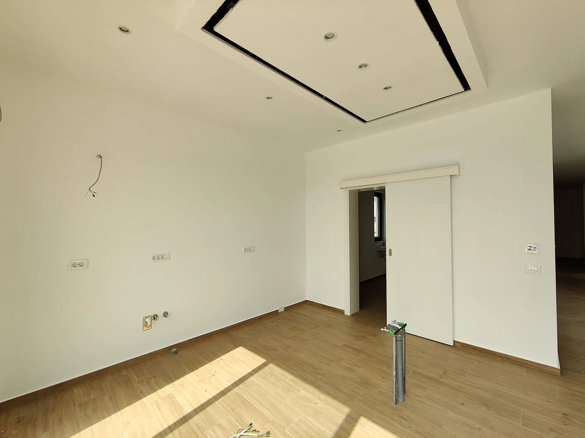 Empty room under renovation with laminate flooring, suspended ceiling, and exposed wiring.