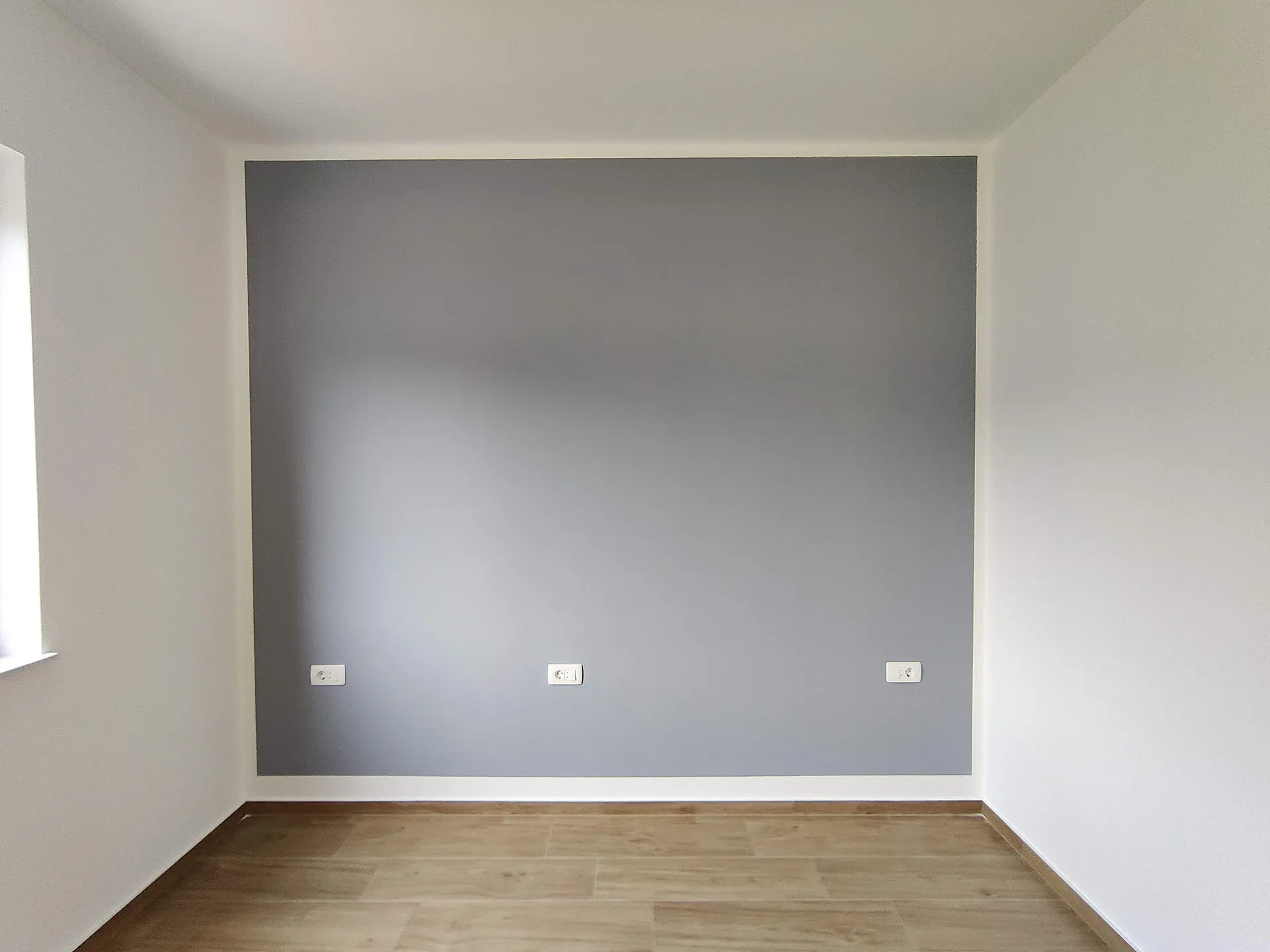 Empty room with a gray accent wall, light laminate flooring, and low electrical outlets. No furniture visible.