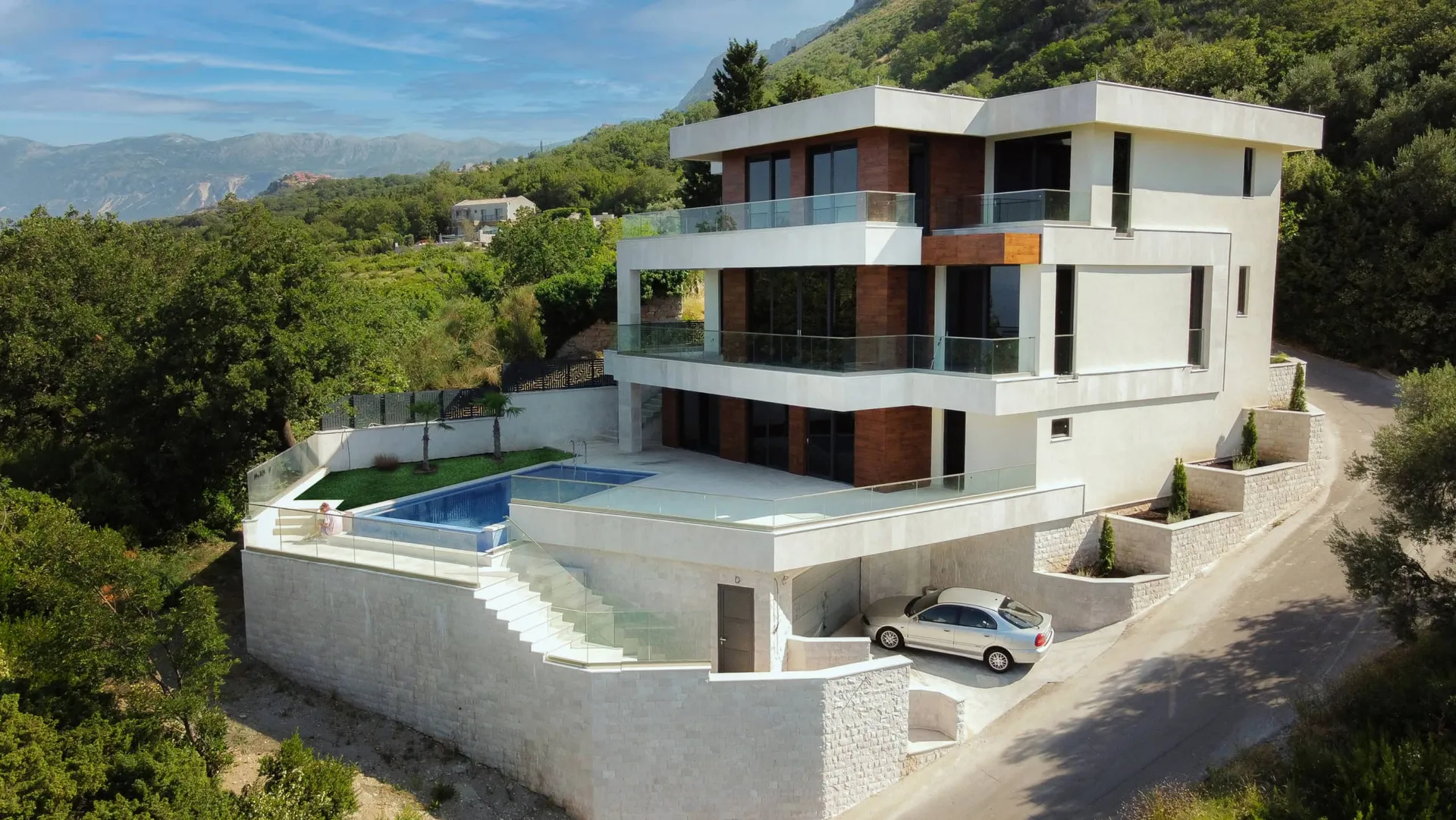 Aerial view of a modern multi-story house with a pool and balconies set against mountains.
