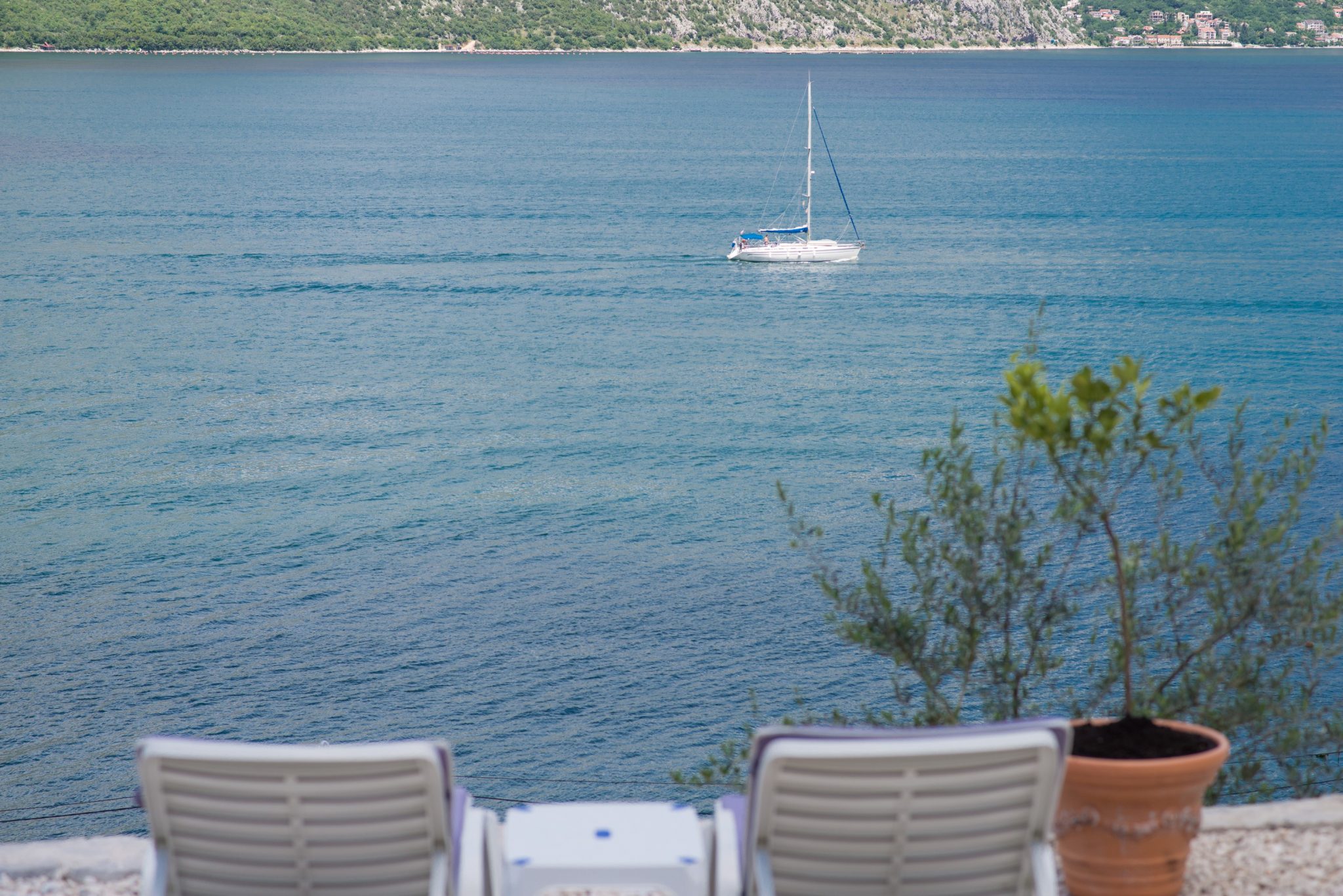 View from the villa terrace in Stoliv, Montenegro: sun loungers, panoramic sea view, and a yacht in the Bay of Kotor.