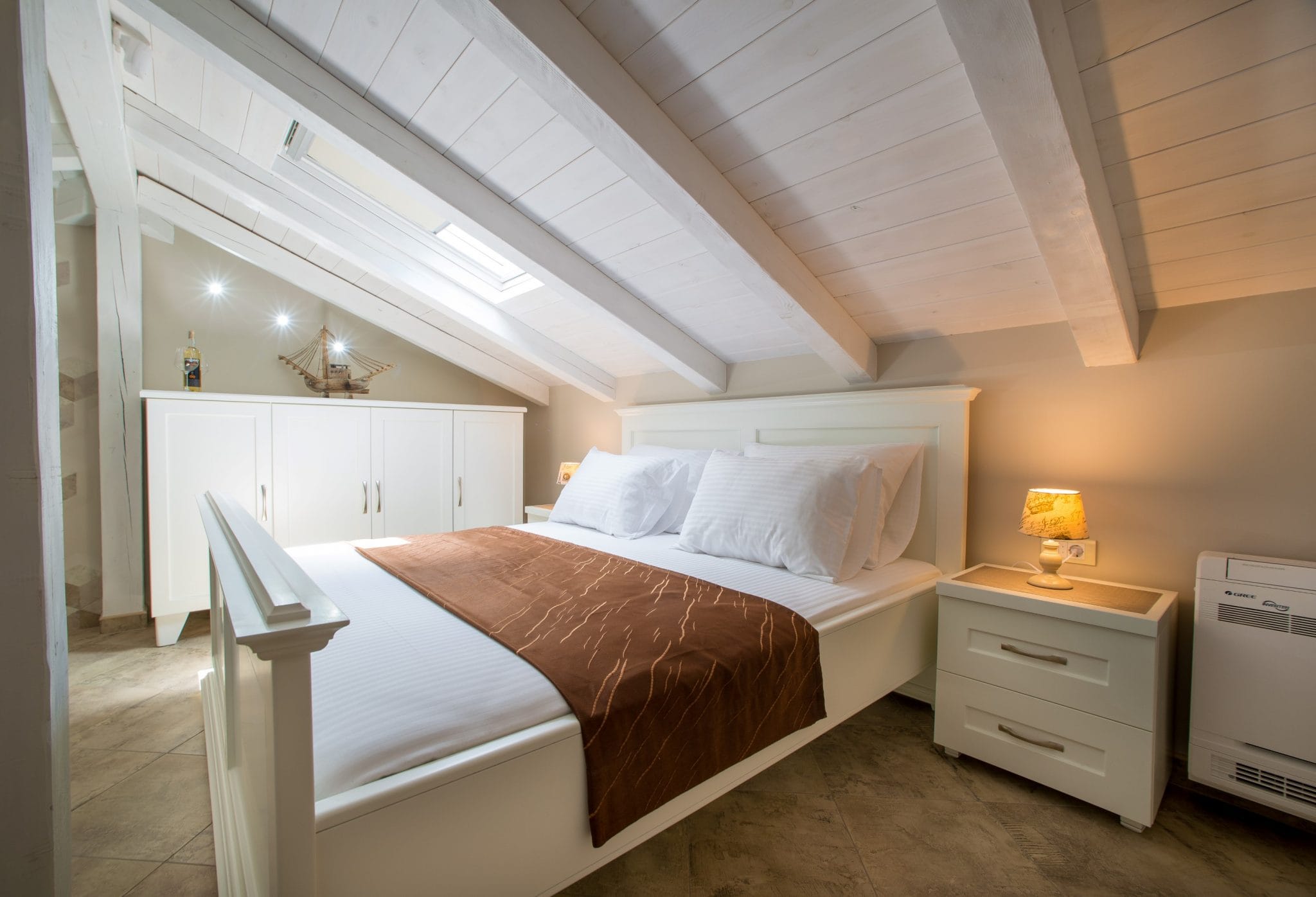 Attic bedroom in a villa in Stoliv, Montenegro: white furniture, a double bed, and ceiling beams.