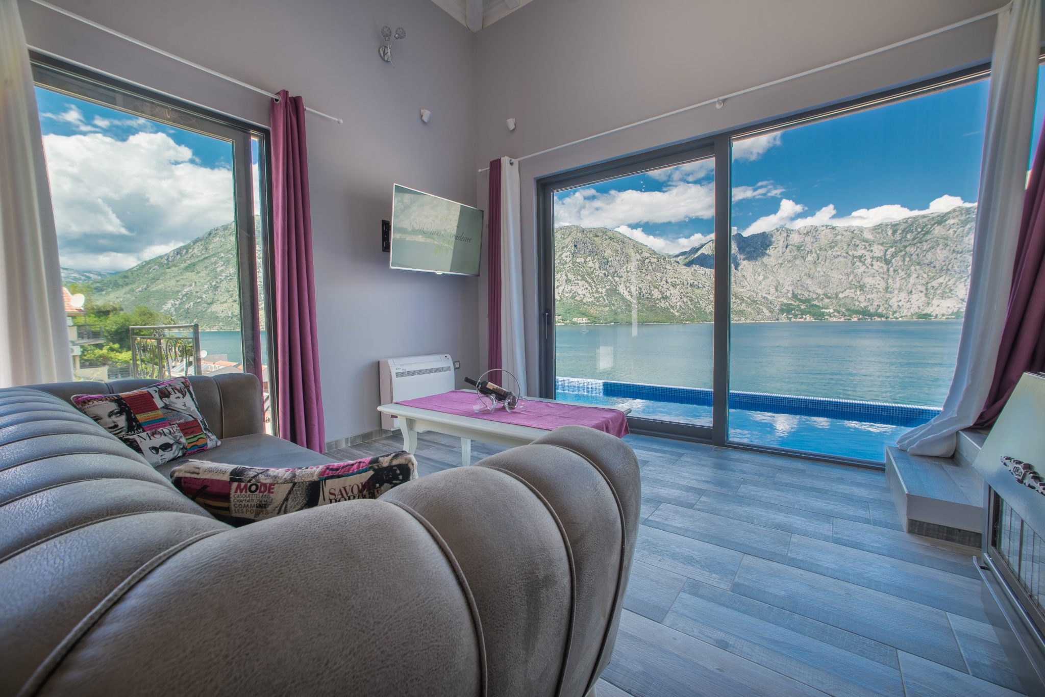 Living room with panoramic windows, sea and mountain views in a villa, Stoliv, Montenegro: modern interior with a pool.