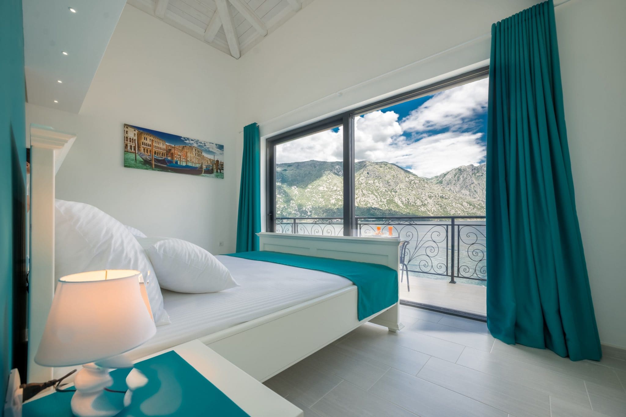 Bedroom in a villa in Stoliv, Montenegro: double bed, panoramic windows with sea and mountain views, balcony.