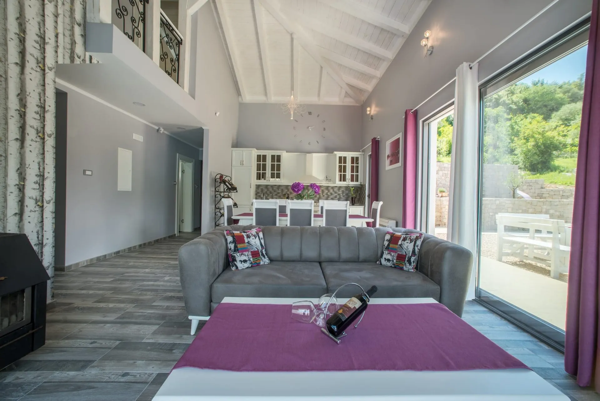 Living room with a grey sofa, fireplace, and open kitchen visible in the background under high ceilings.