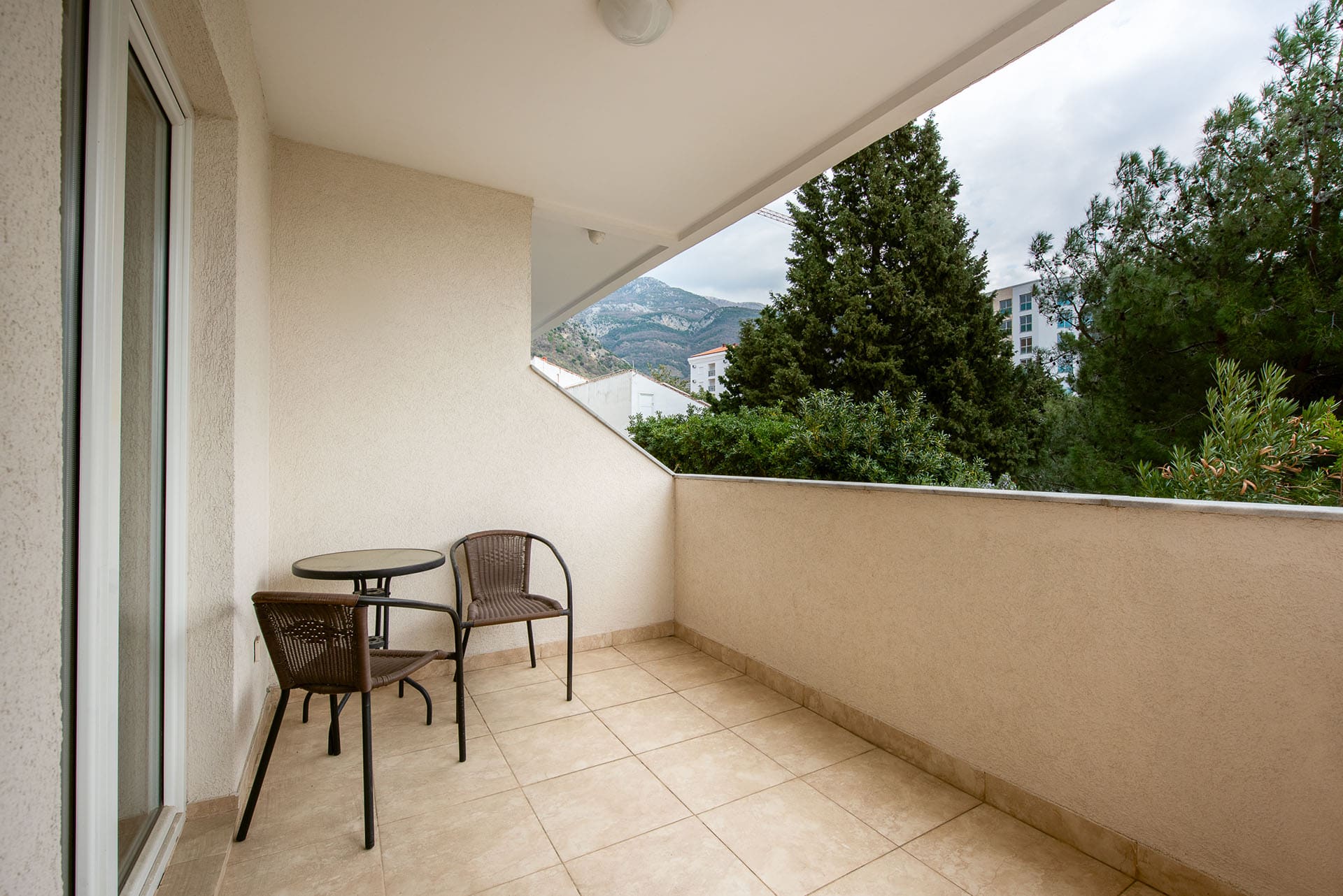 Cozy balcony with wicker furniture and mountain views in an apartment in Bečići, Montenegro. Tiled floor, light finishes.