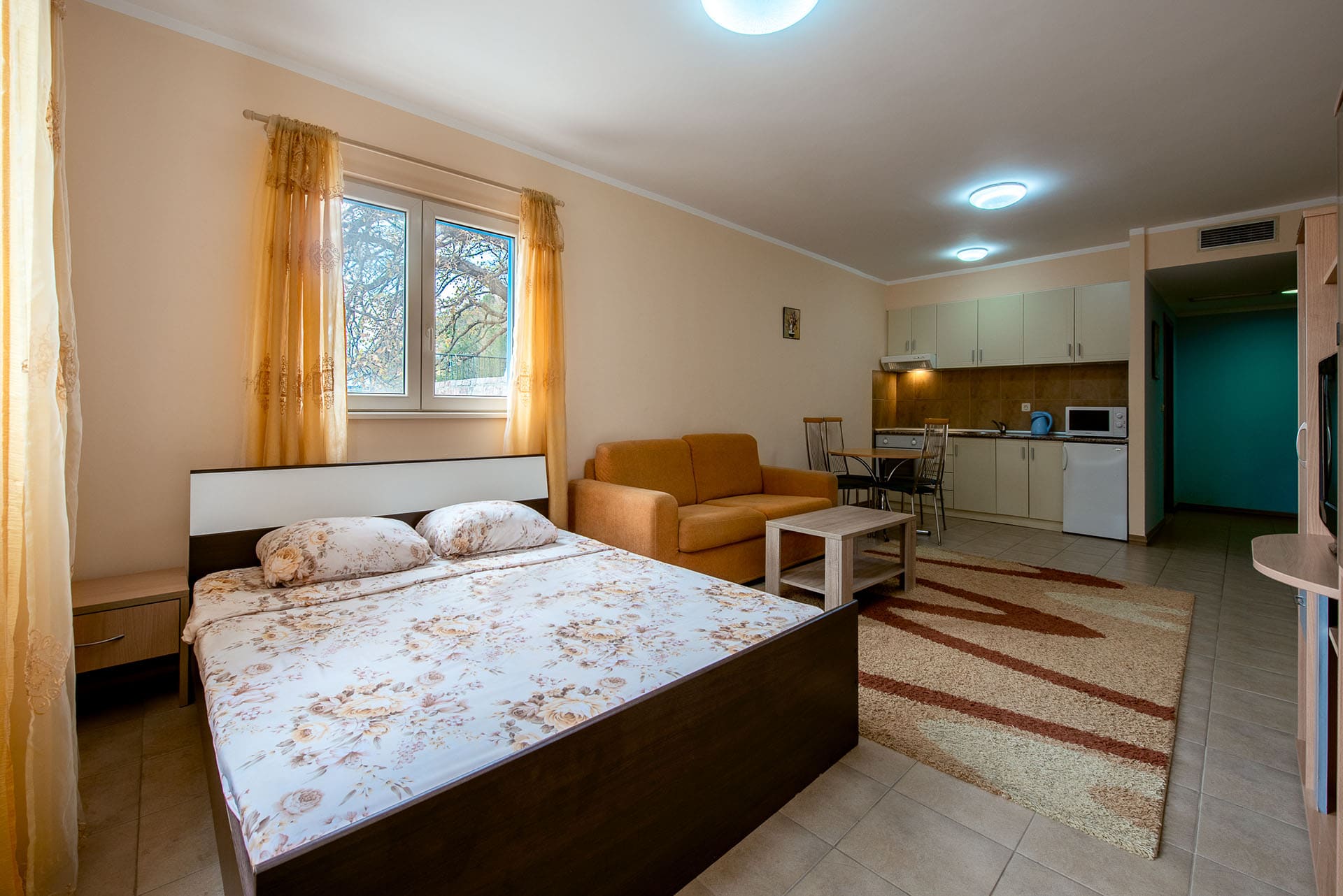 Living room interior with a double bed and kitchen in an apartment in Bečići, Montenegro: cozy furniture and a view from the window.