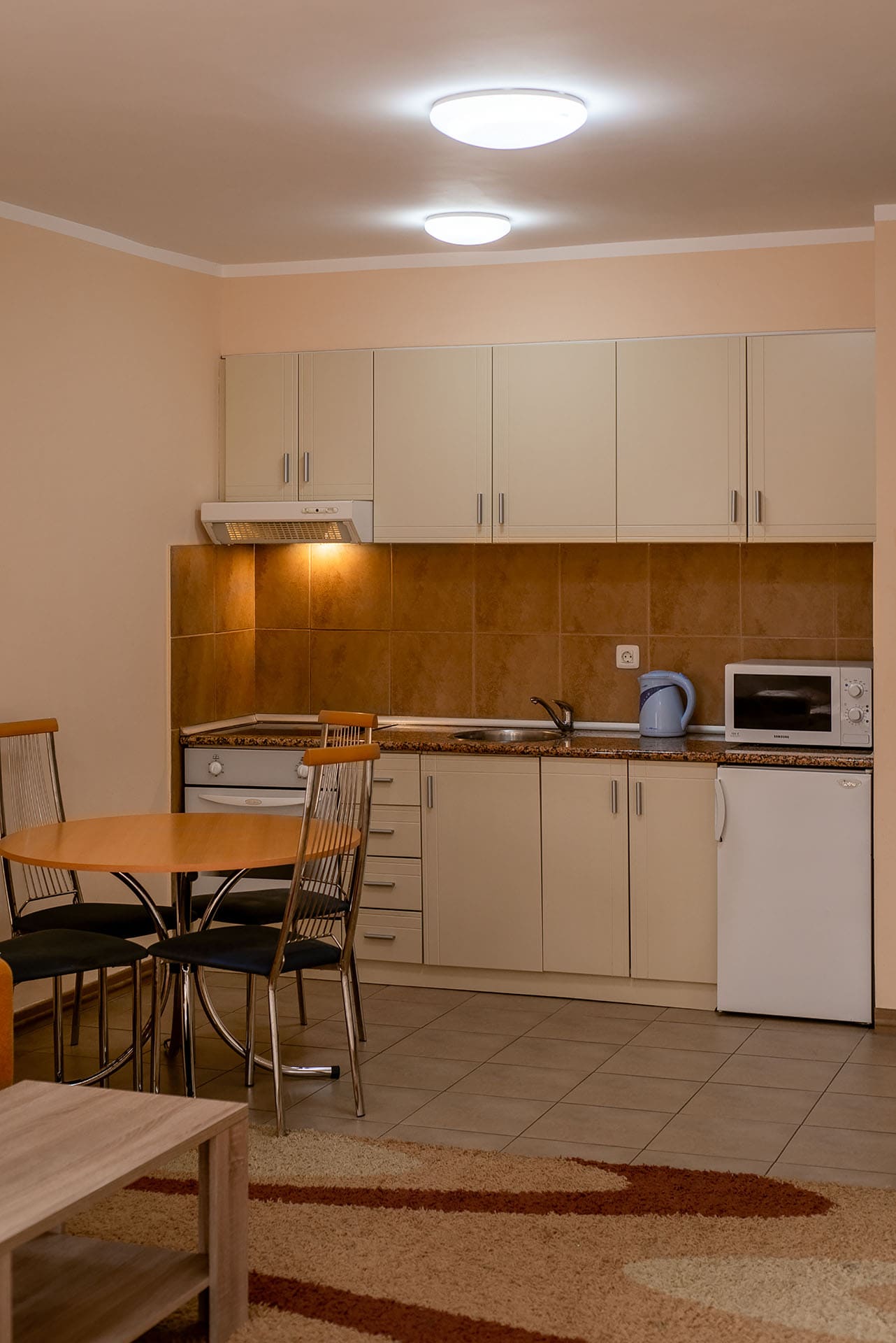 Kitchen in an apartment in Bečići, Montenegro: light-colored cabinets, dining table, built-in appliances, and tiled backsplash.