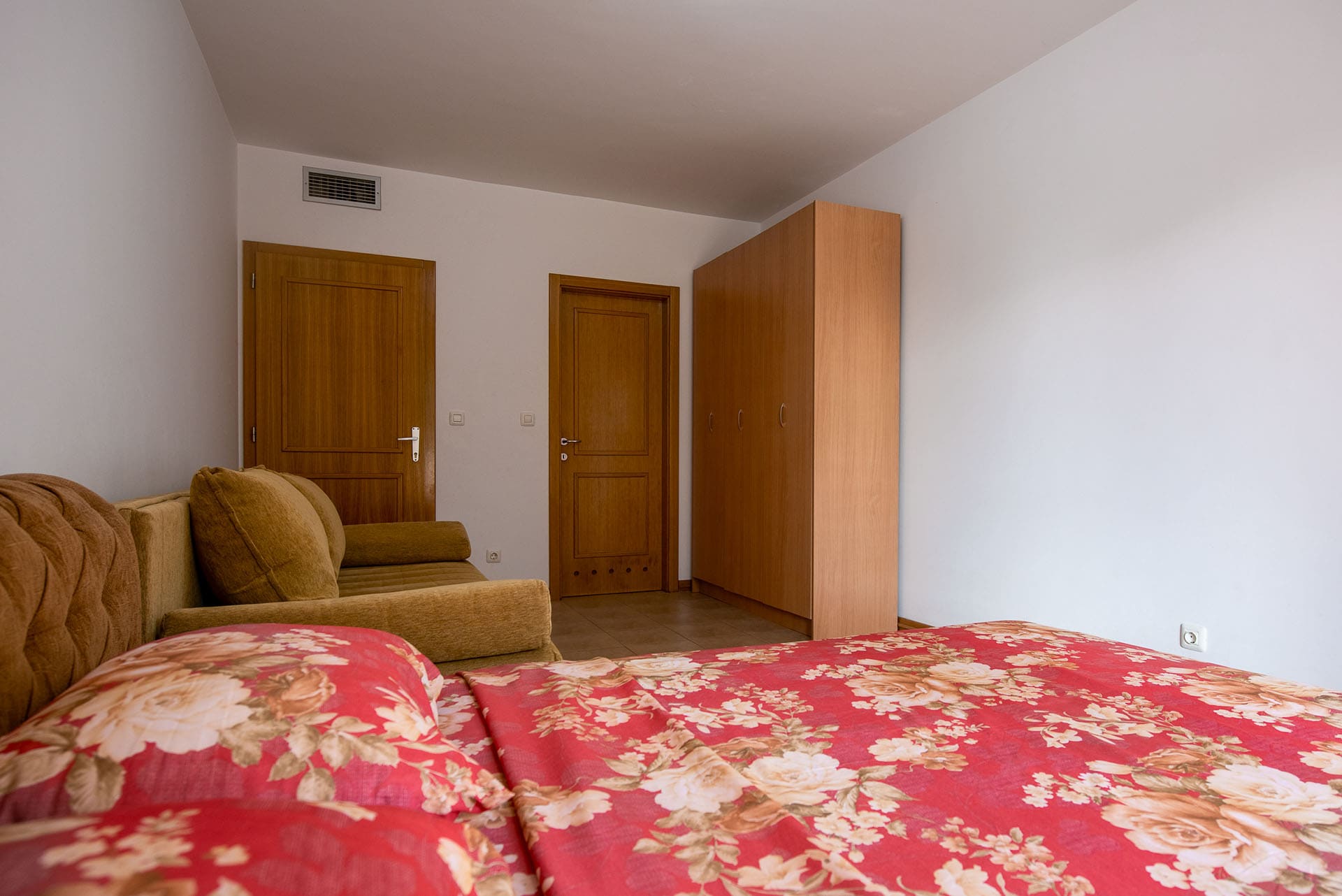 Bedroom in an apartment in Bečići, Montenegro: double bed, soft sofa, wardrobe, and wooden interior doors.