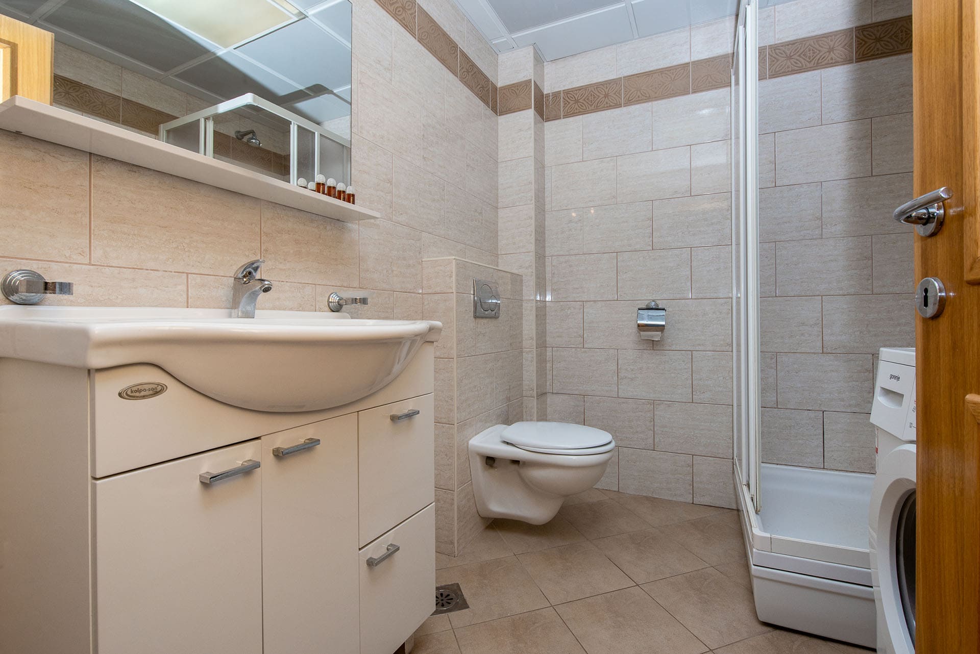 Bathroom in an apartment in Bečići, Montenegro: shower cabin, wall-mounted toilet, vanity with sink, and light-colored tiles.