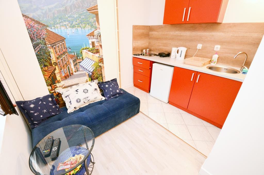 Living room with kitchen in a house in Kotor, Montenegro: a blue sofa, a bright kitchen set, and a mural with a seascape.