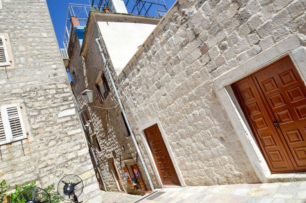 A narrow street in the old town of Kotor, Montenegro: traditional stone houses with wooden doors and white shutters.