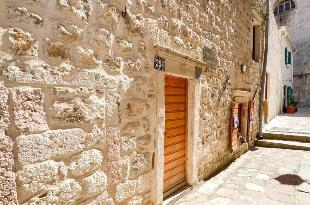 Stone wall with a wooden door and number 396 on a narrow cobblestone street.