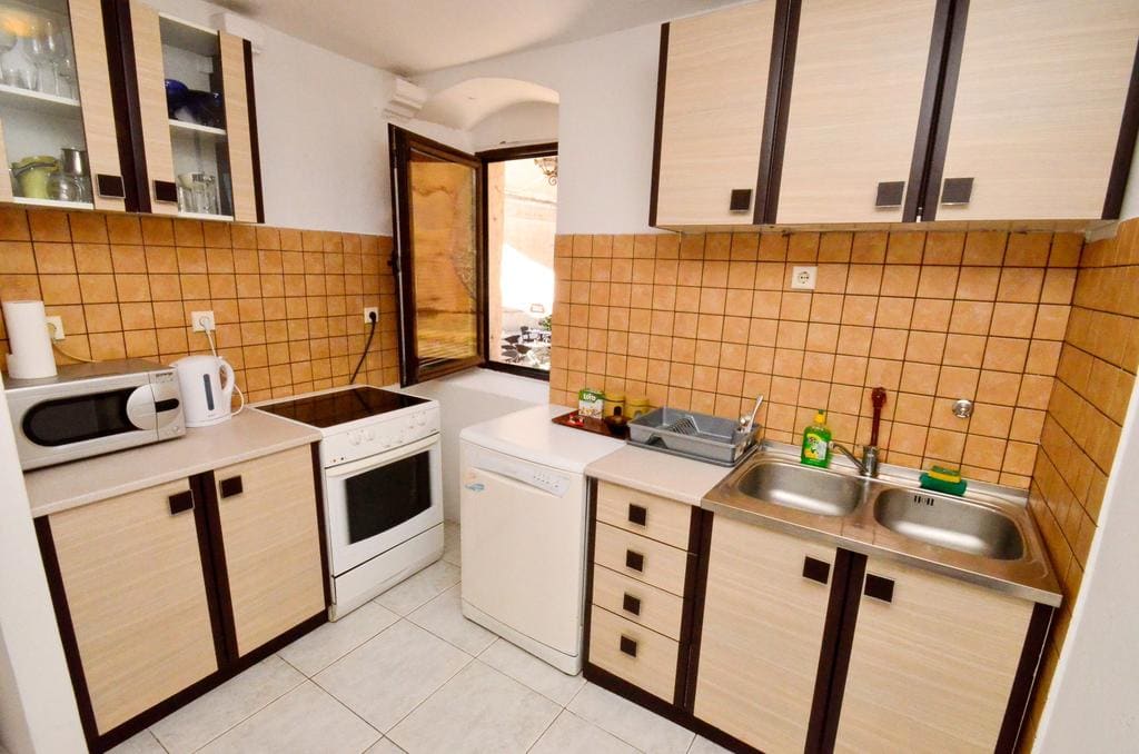 Bright kitchen in a house in Kotor, Montenegro: beige cabinets, tiled backsplash, sink, and appliances.