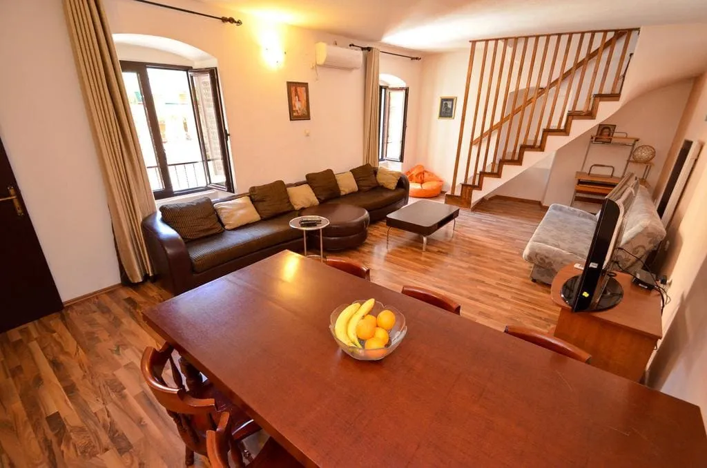 Living room with sofa, dining table, wooden stairs and TV set.