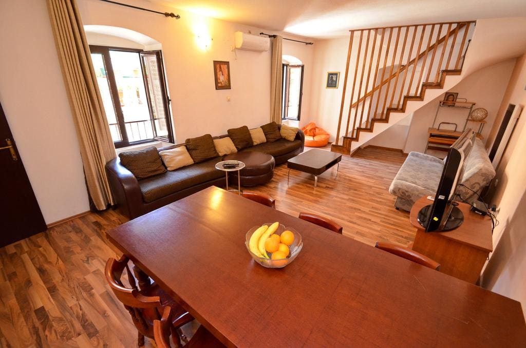 Living room with a wooden staircase and dining area in a house in Kotor, Montenegro: leather sofa and parquet floor.