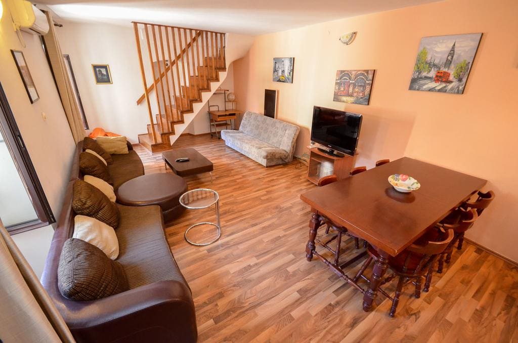 Living room with a wooden staircase and dining area in a house in Kotor, Montenegro: soft seating, TV, and parquet flooring.