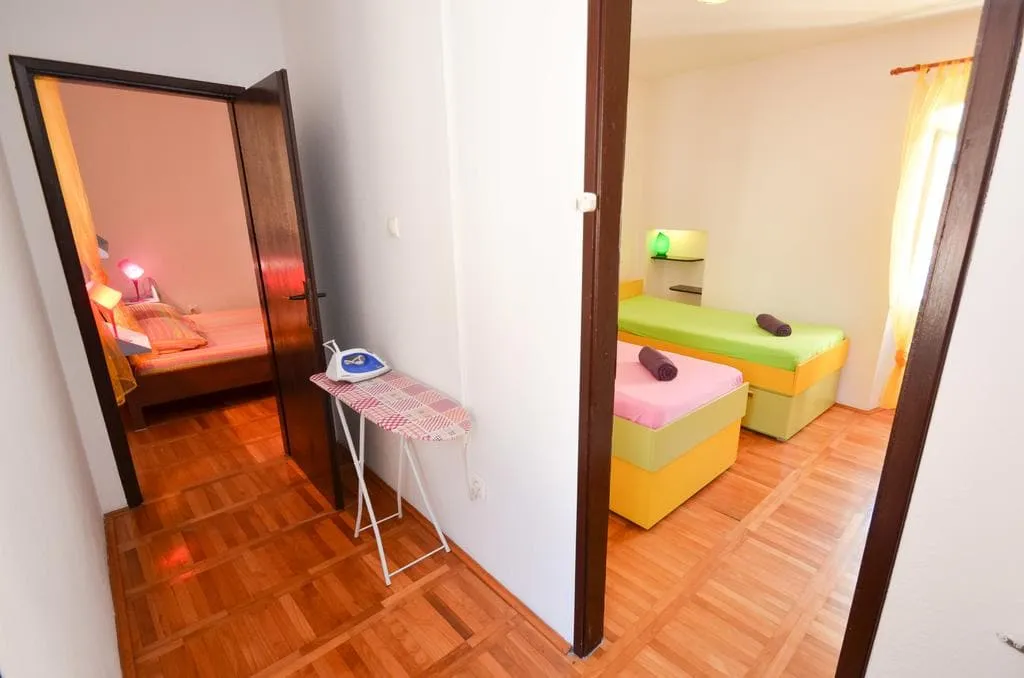 Hallway with ironing board, views into two bedrooms: one with a double bed, another with two single beds.