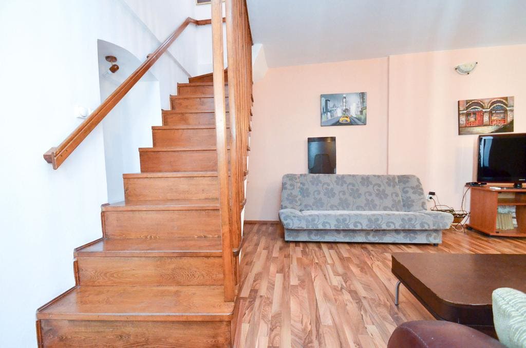 Living room with a wooden staircase and upholstered furniture in a house, Kotor, Montenegro. Interior with laminate flooring and a TV area.