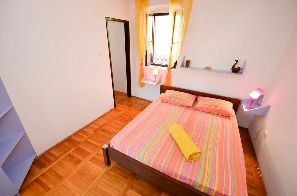 Bedroom with a double bed in striped bedding, wooden parquet floor, yellow curtains, and wall-mounted lamps.