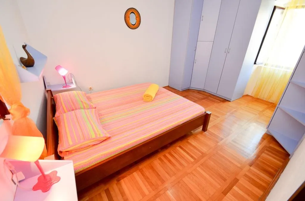 Bedroom with a wooden bed in striped bedding, white wardrobe, and parquet flooring.