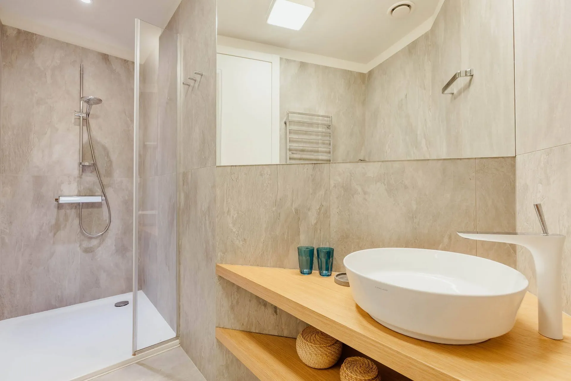 Modern bathroom featuring a glass shower stall, white vessel sink on a wooden counter, and beige tiles.
