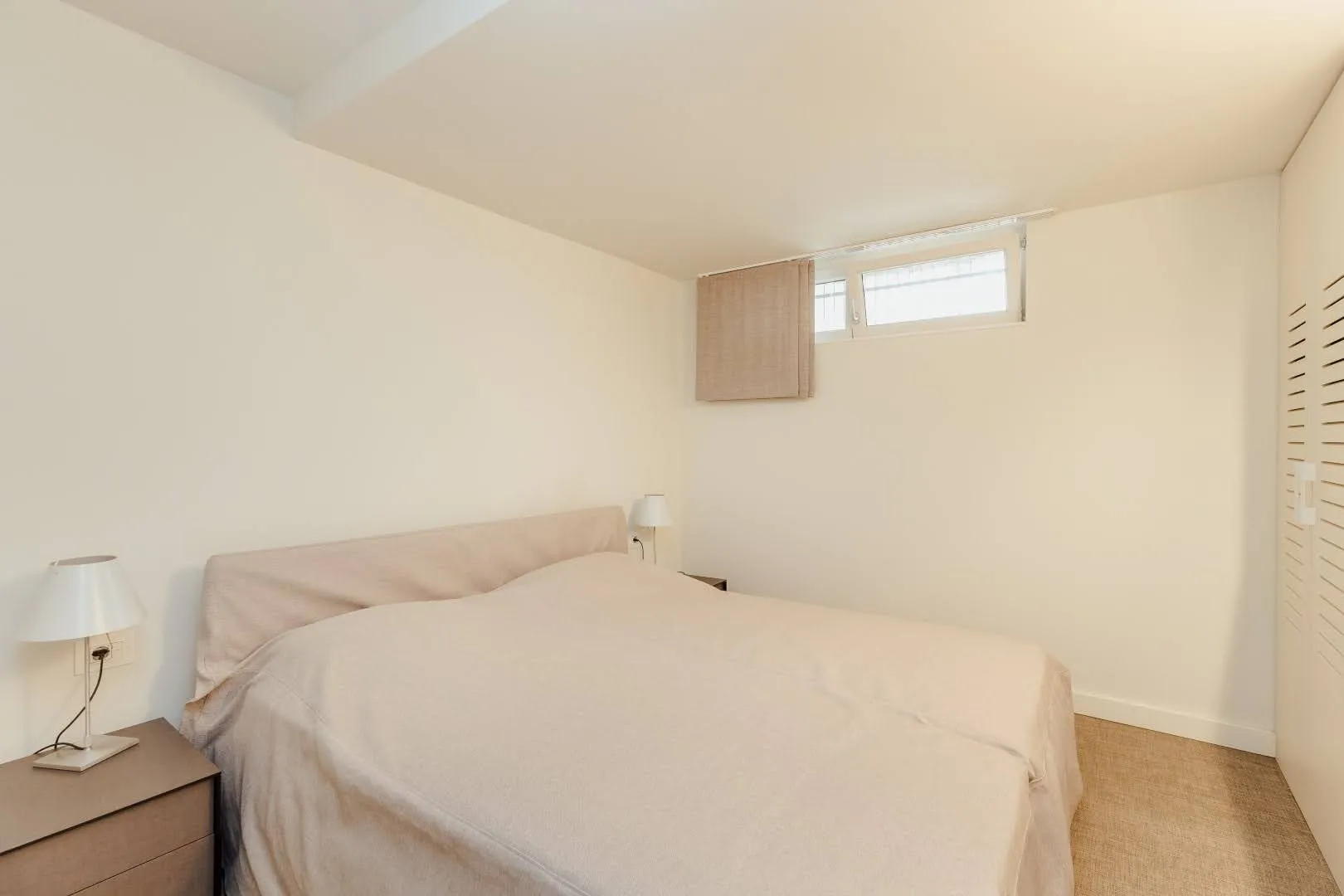 Bedroom featuring a double bed in beige tones, a nightstand with a lamp, and louvered closet doors.