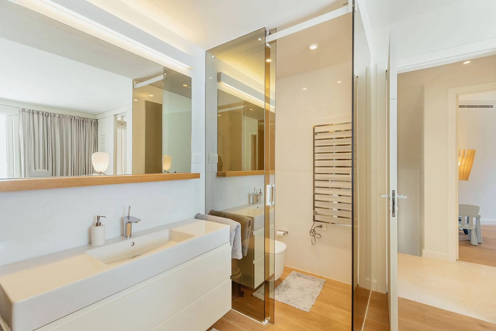 Modern bathroom featuring a white vanity sink, large mirror, glass partition, and heated towel rail.