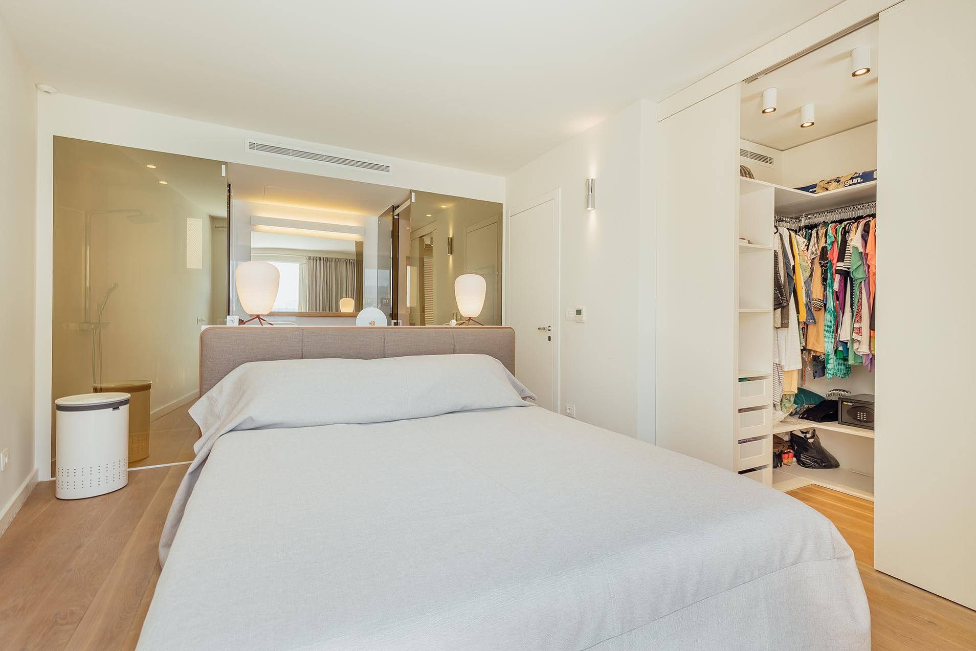 Modern bedroom featuring a double bed, open walk-in closet with clothes, and a large mirror.