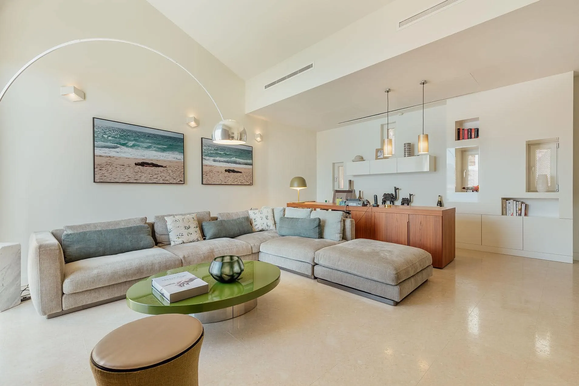 Bright living room with a gray sectional sofa, green coffee table, and large arched lamp.