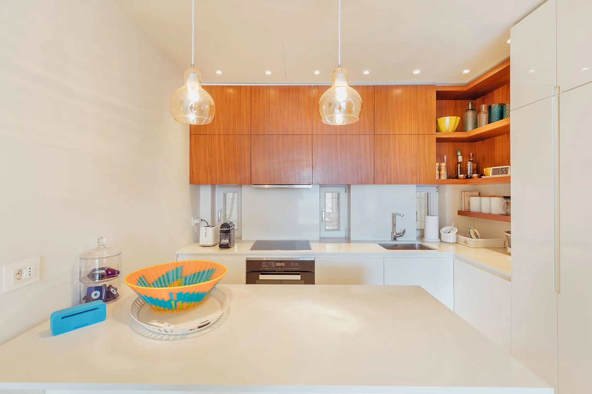 Modern kitchen featuring wood cabinets, white countertops, built-in appliances, sink, and pendant lights.