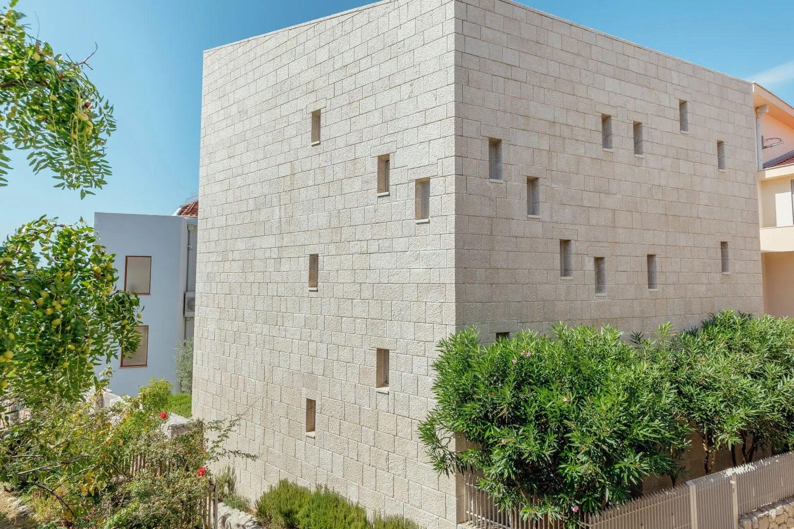 Exterior view of a multi-story building with light stone masonry and narrow windows against a blue sky.