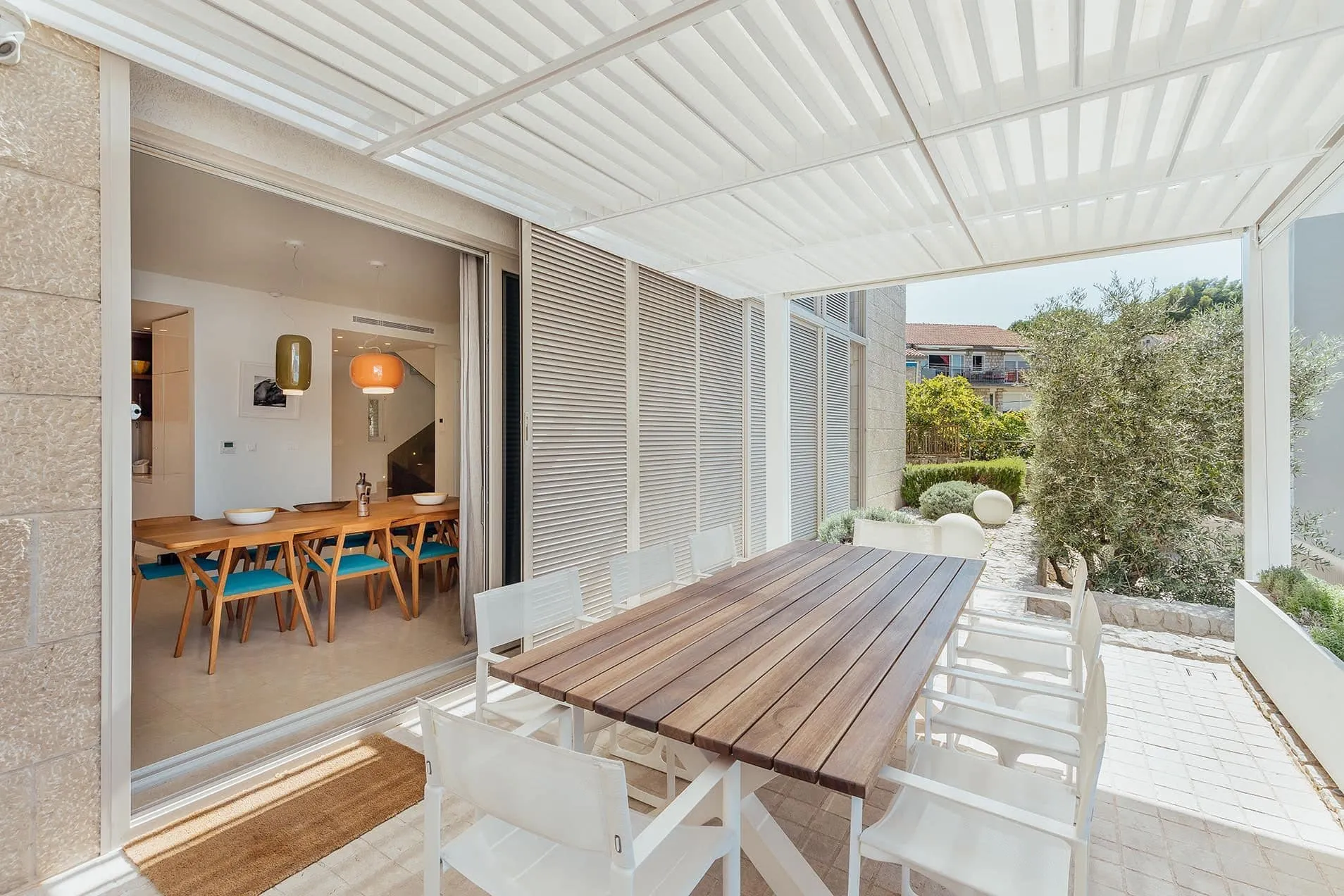 Covered terrace with a wooden table and white chairs, adjacent dining area visible through sliding doors.