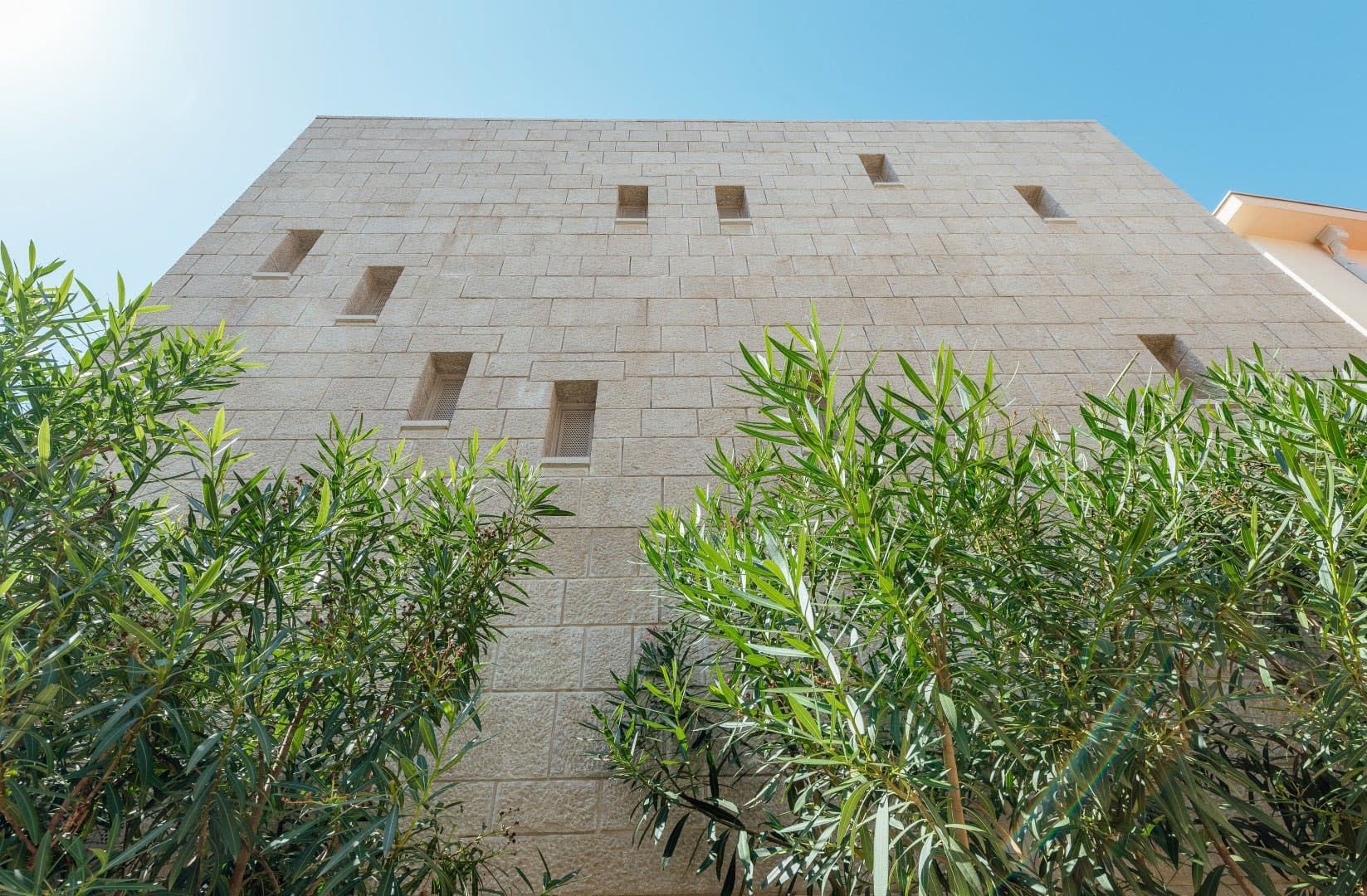 Facade of a modern villa made of light stone in Pržno, Montenegro, against a backdrop of a green garden and clear sky.