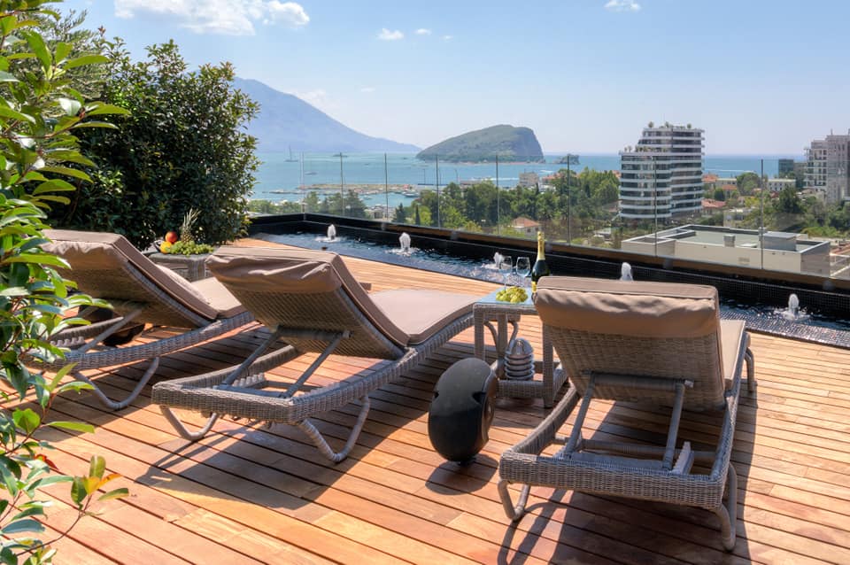 Penthouse terrace in Budva, Montenegro: sun loungers, a pool with fountains, and panoramic views of the sea and St. Nicholas Island.